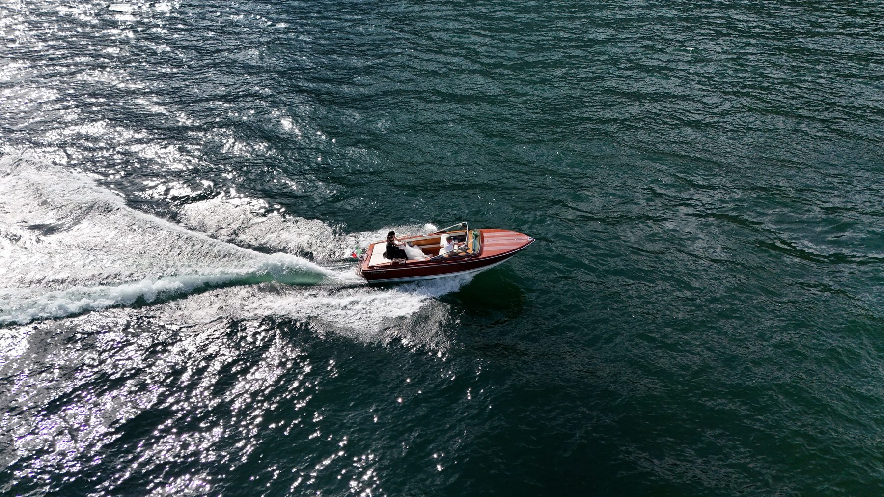 A wooden boat crossing Lake Como, the wake behind it